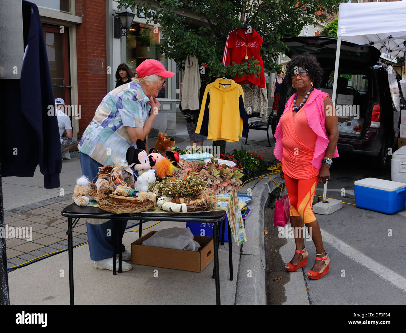 A mature black woman wearing brightly coloured clothing browses a charity stall at a farmers market in Milton, Ontario, Canada Stock Photo