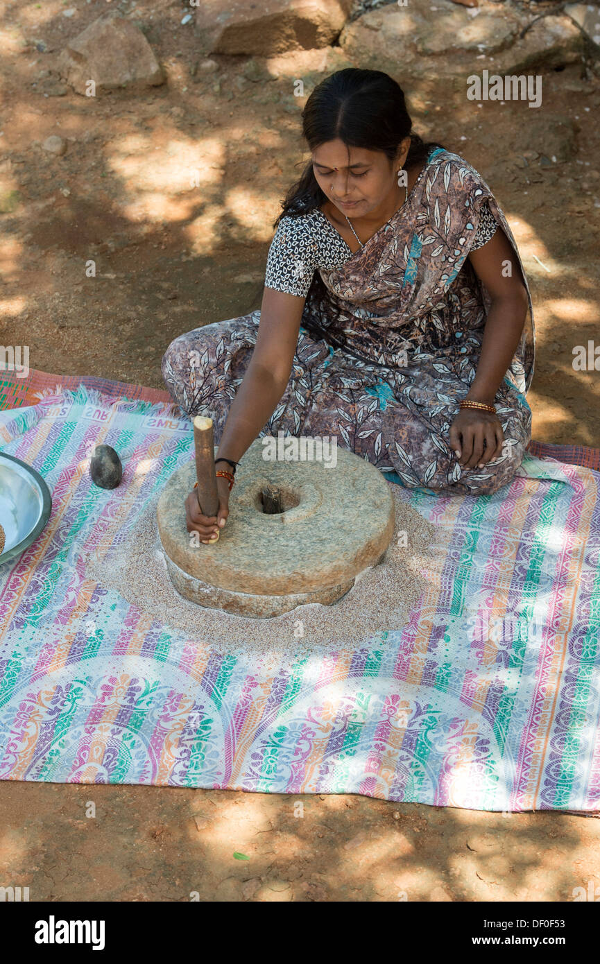 Rural Indian village woman using Quern stones to grind Finger Millet seed / Ragi seeds into Ragi flour. Andhra Pradesh. India Stock Photo