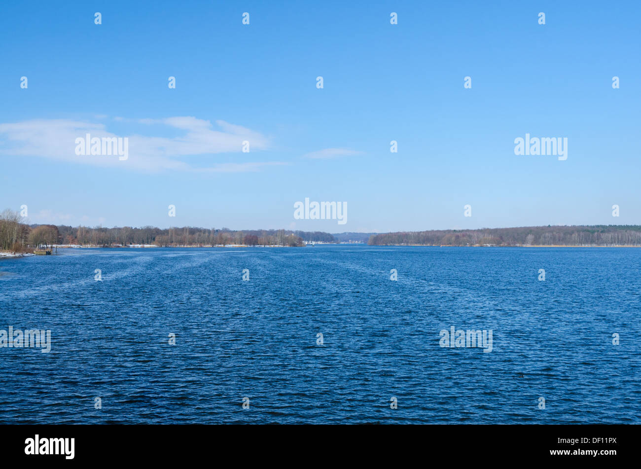 Deep blue water surface of european lake or river and snowy forest on skyline Stock Photo
