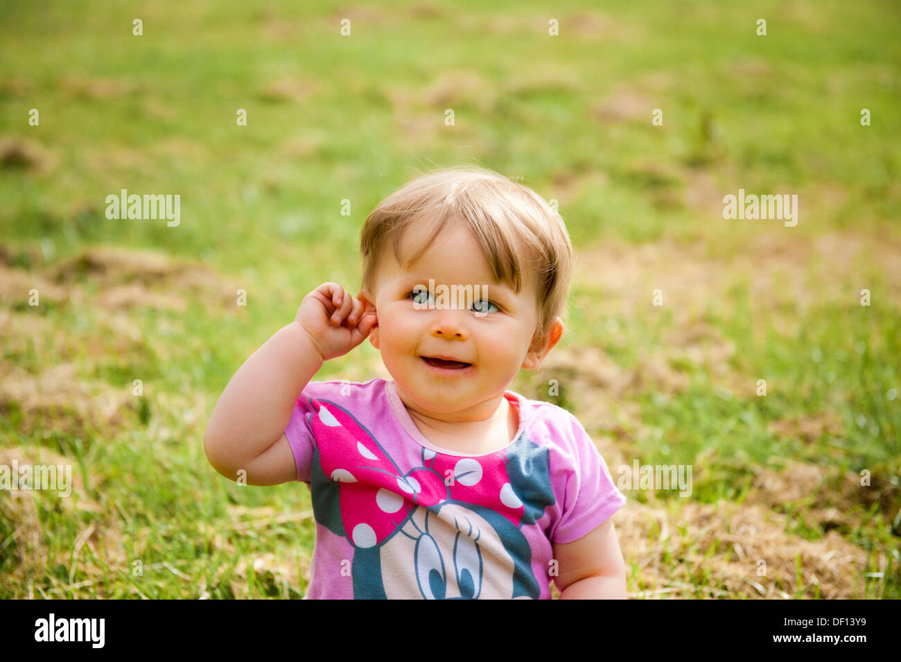 baby sitting on grass holding her ear and smiling Stock Photo - Alamy
