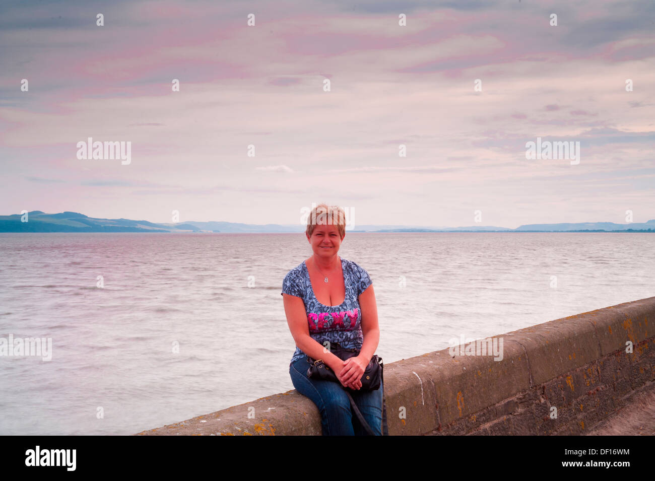 Woman sitting on sea wall at sunset Stock Photo - Alamy