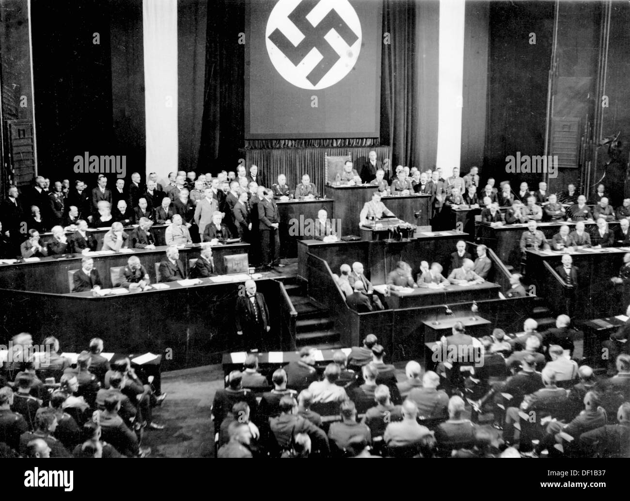 The image from the Nazi Propaganda! shows Reich Chancellor Adolf Hitler delivering a speech to the Reichstag in the Kroll Opera House in Berlin, Germany, 17 May 1933. To the left, first row (r-l): Vice Chancellor Franz von Papen, Foreign Minister Konstantin von Neurath, Reich Minister of the Interior Wilhelm Frick; second row (r-l): Minister of Economics and Agriculture Alfred Hugenberg, Minister for Labour Franz Seldte, Minister of War Werner von Blomberg. Behind Hitler, Hermann Göring. Fotoarchiv für Zeitgeschichte Stock Photo