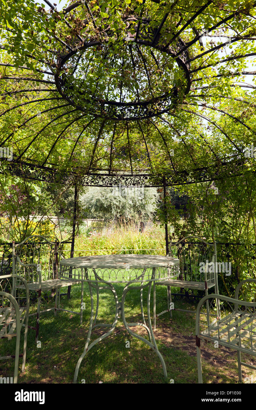 Large metal, plant covered, Gazebo, containg garden furniture in the