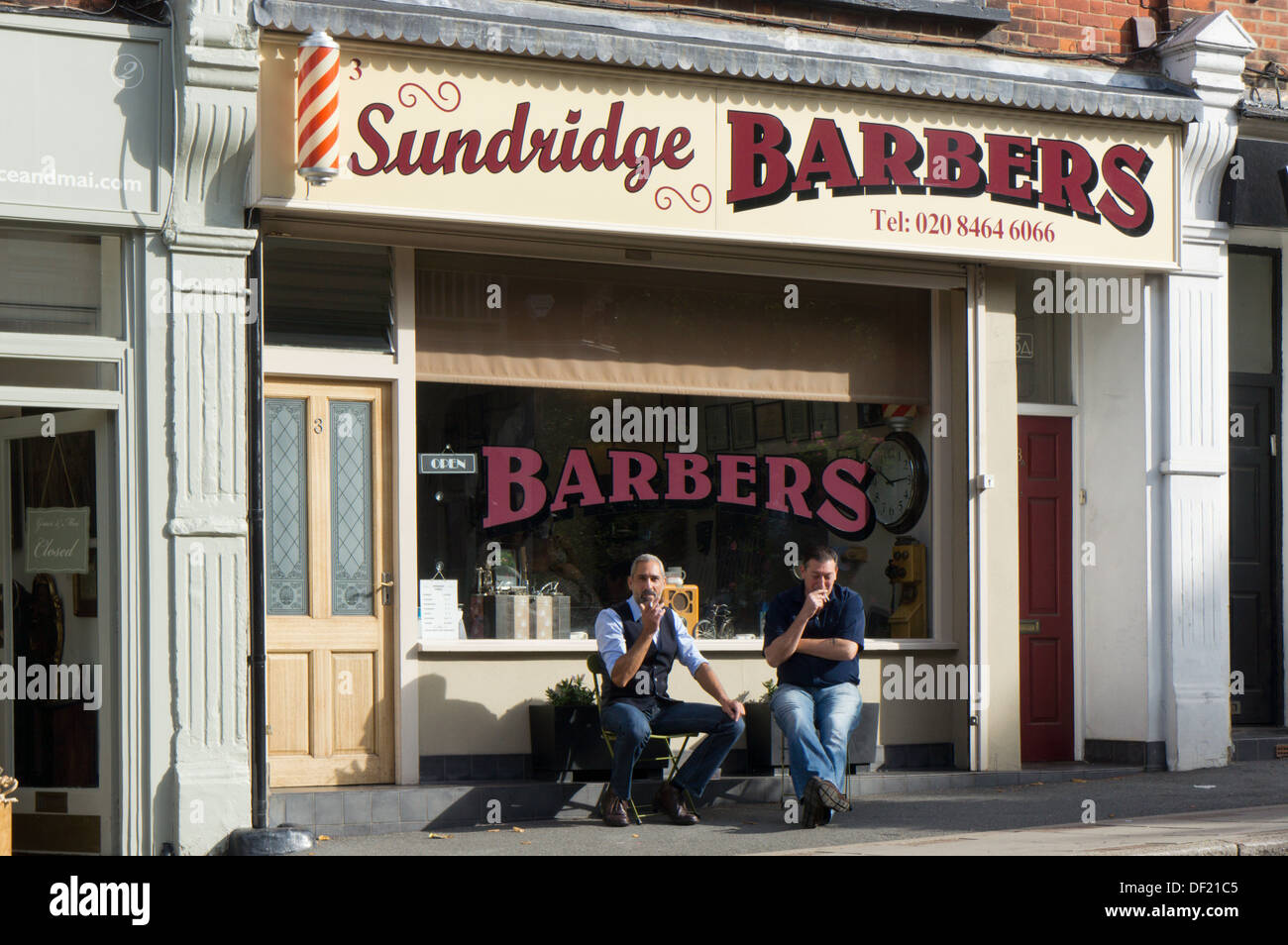 Two men relaxing sitting in the sun outside a barber's shop. Stock Photo