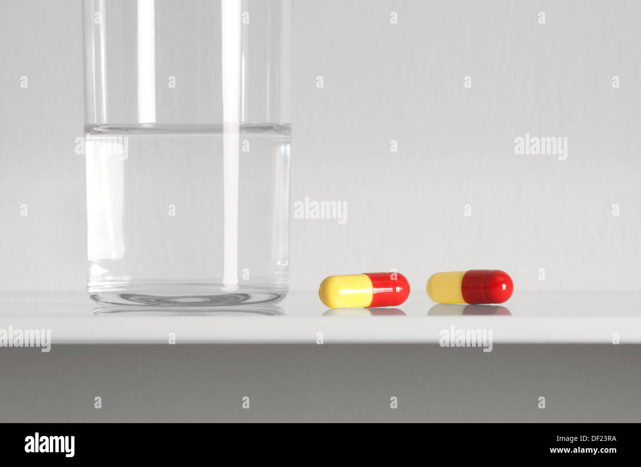 capsules and glass of water on white shelf Stock Photo