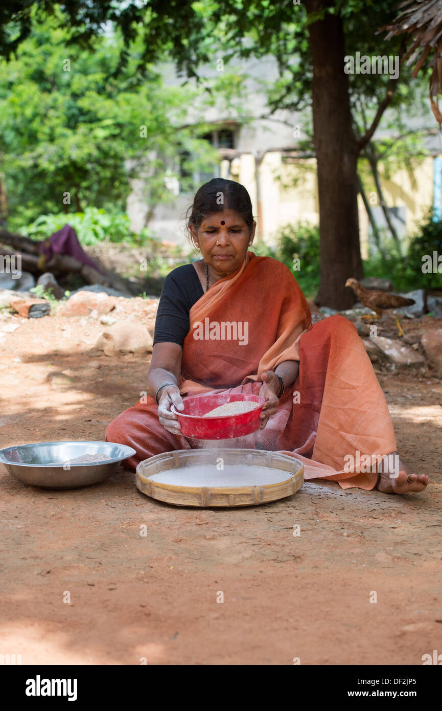 Rural Indian village woman sifting Finger Millet flour / Ragi flour after grinding. Andhra