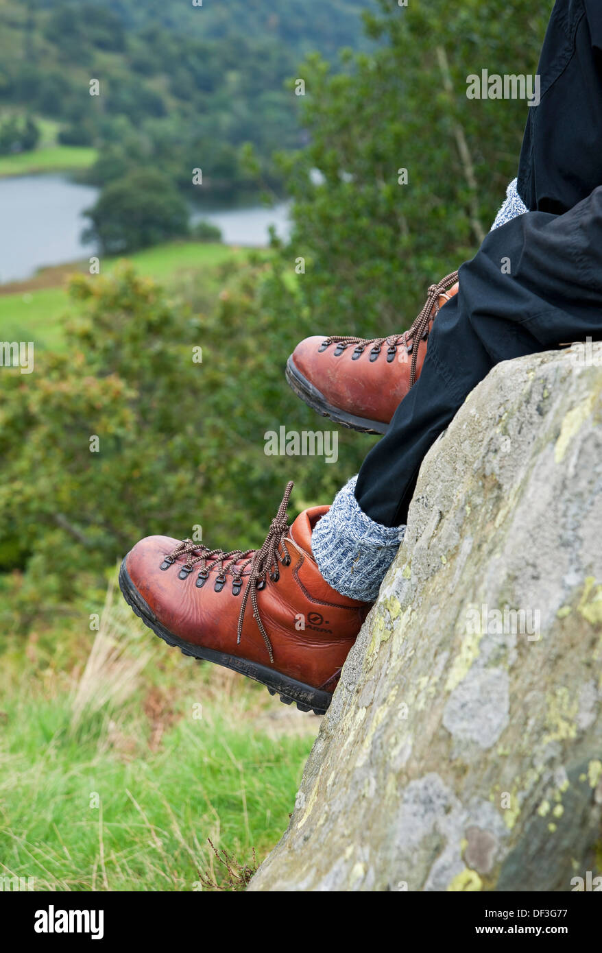Close up of man person walker sitting resting on a rock in wearing walking boots Lake District National Park England UK United Kingdom Great Britain Stock Photo