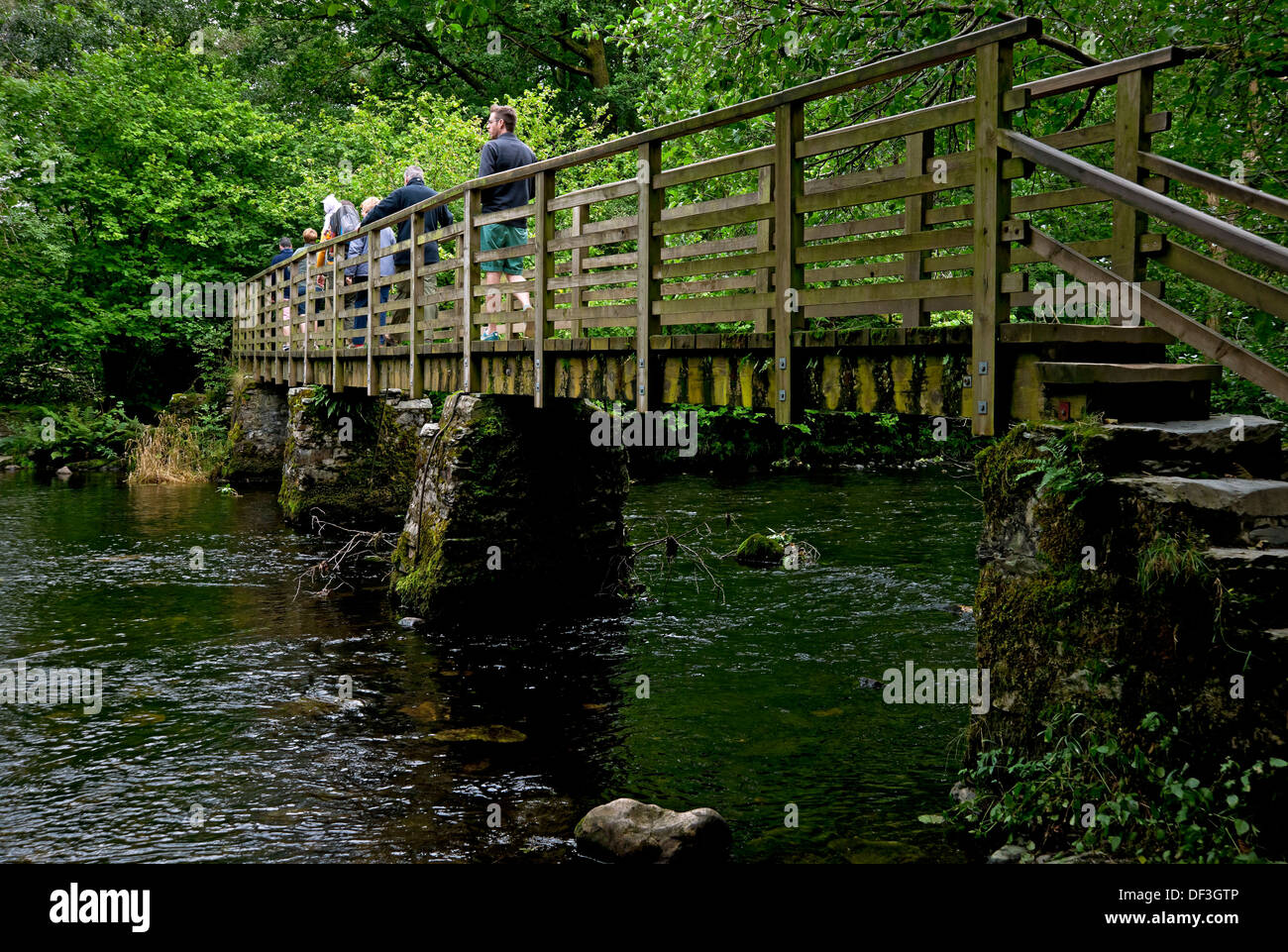 Visitors people crossing wooden footbridge bridge walking across River Rothay in summer near Grasmere Cumbria England UK United Kingdom Great Britain Stock Photo
