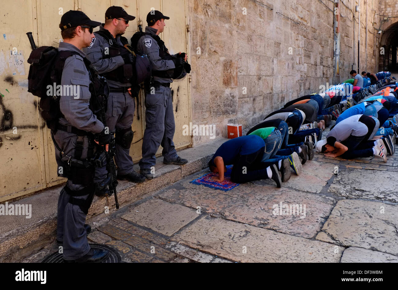 Armed Israeli border policemen stand guard next to Palestinians who were banned to enter Akza mosque and are praying in the Muslim Quarter of the Old City of Jerusalem on 27 September 2013. Israeli authorities have imposed severe restrictions on Muslim worshippers who want to perform Friday prayer in the Noble Sanctuary. The police allowed Palestinian men over 50 year to enter mosque along with women and children.  Credit:  Eddie Gerald/Alamy Live News Stock Photo