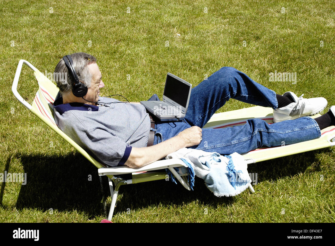 Senior male relaxes outside in a chair while watching a portable DVD player Stock Photo