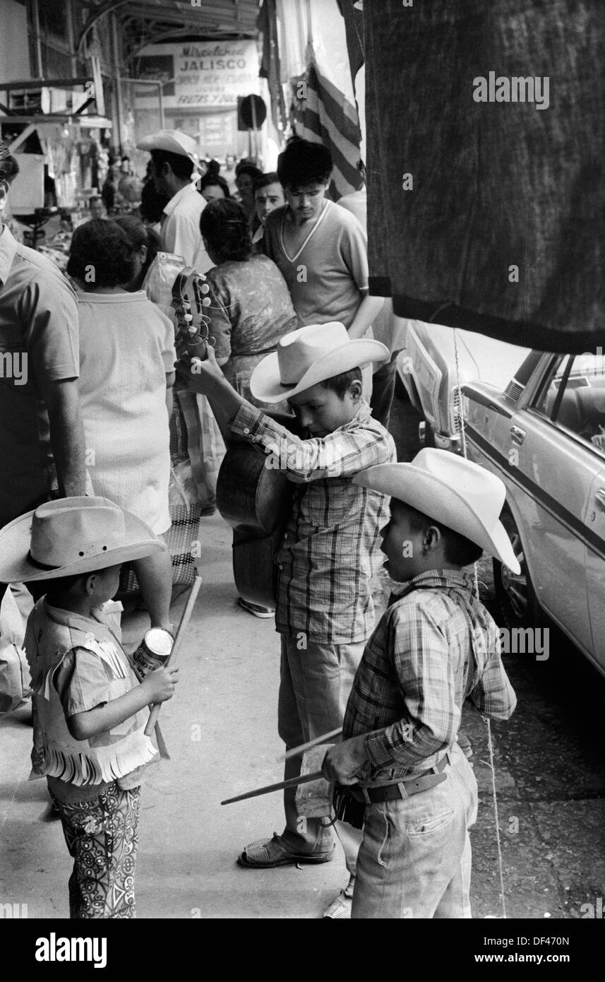 Mazatlan Mexico 1970s. Children busking in the crowded street, brother young sibling  playing a simple wooden percussion block and the youngest is playing on a tin can.  Mexican state of Sinaloa 1973. HOMER SYKES Stock Photo
