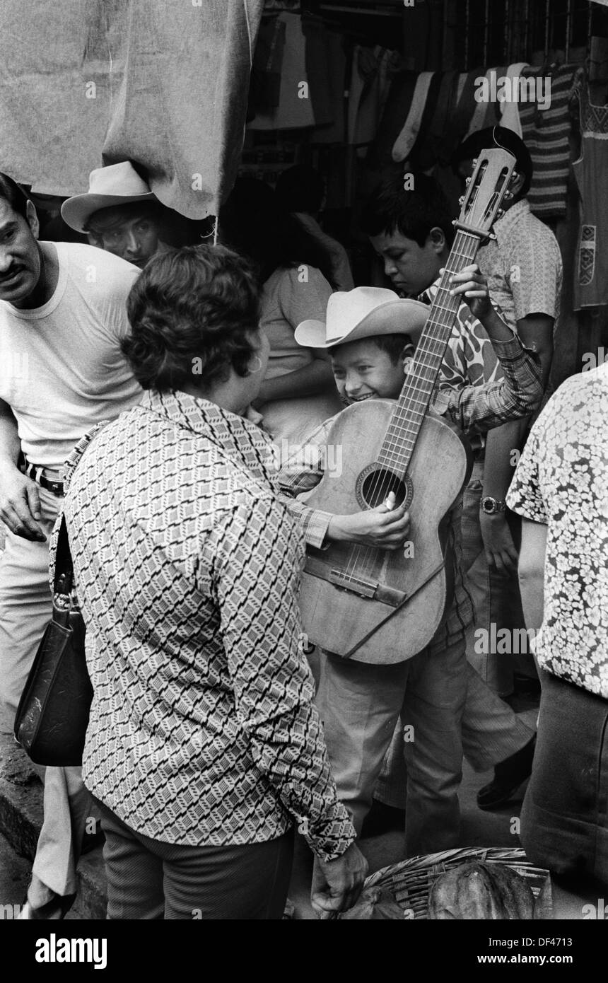 Mazatlan Mexico, young boy busking in the crowded street playing the guitar 1970s Mexican state of Sinaloa. 1973  HOMER SYKES Stock Photo