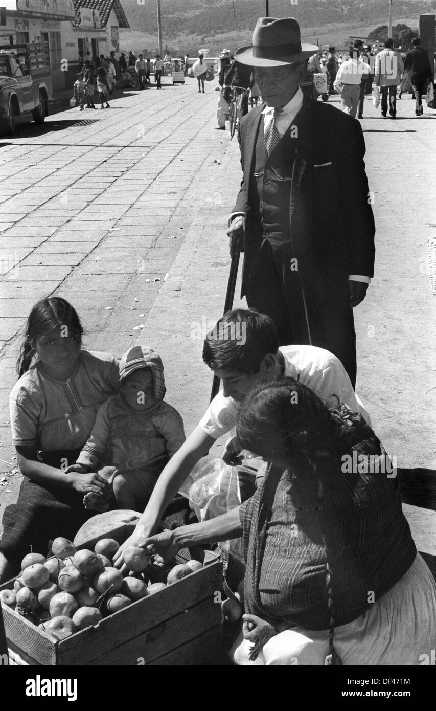 San Cristóbal de las Casas 1970s Mexico. Elderly man has servant  to buy fruit for him from Indigenous young Indian girls with a baby selling in the daily market. Mexican State of Chipas. 1973 HOMER SYKES Stock Photo