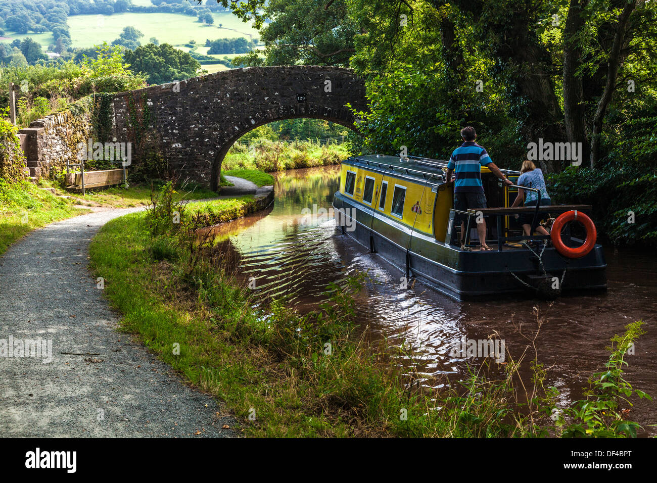 Narrowboat passes under stone bridge over the Monmouthshire and Brecon Canal at Llangynidr in the Brecon Beacons National Park. Stock Photo