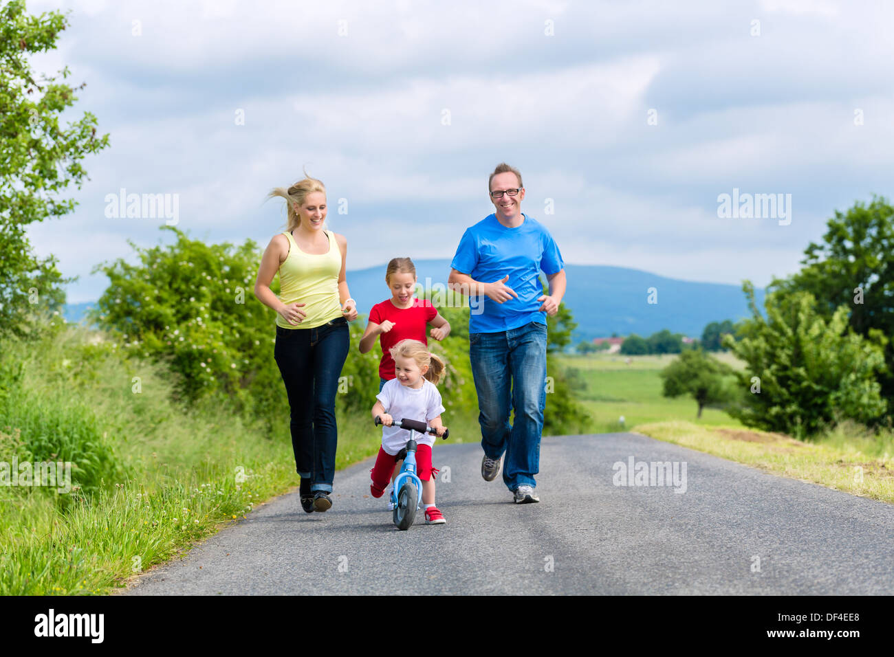 Family of Little girl father and mother or mom and dad running on street in rural environment for sport Stock Photo