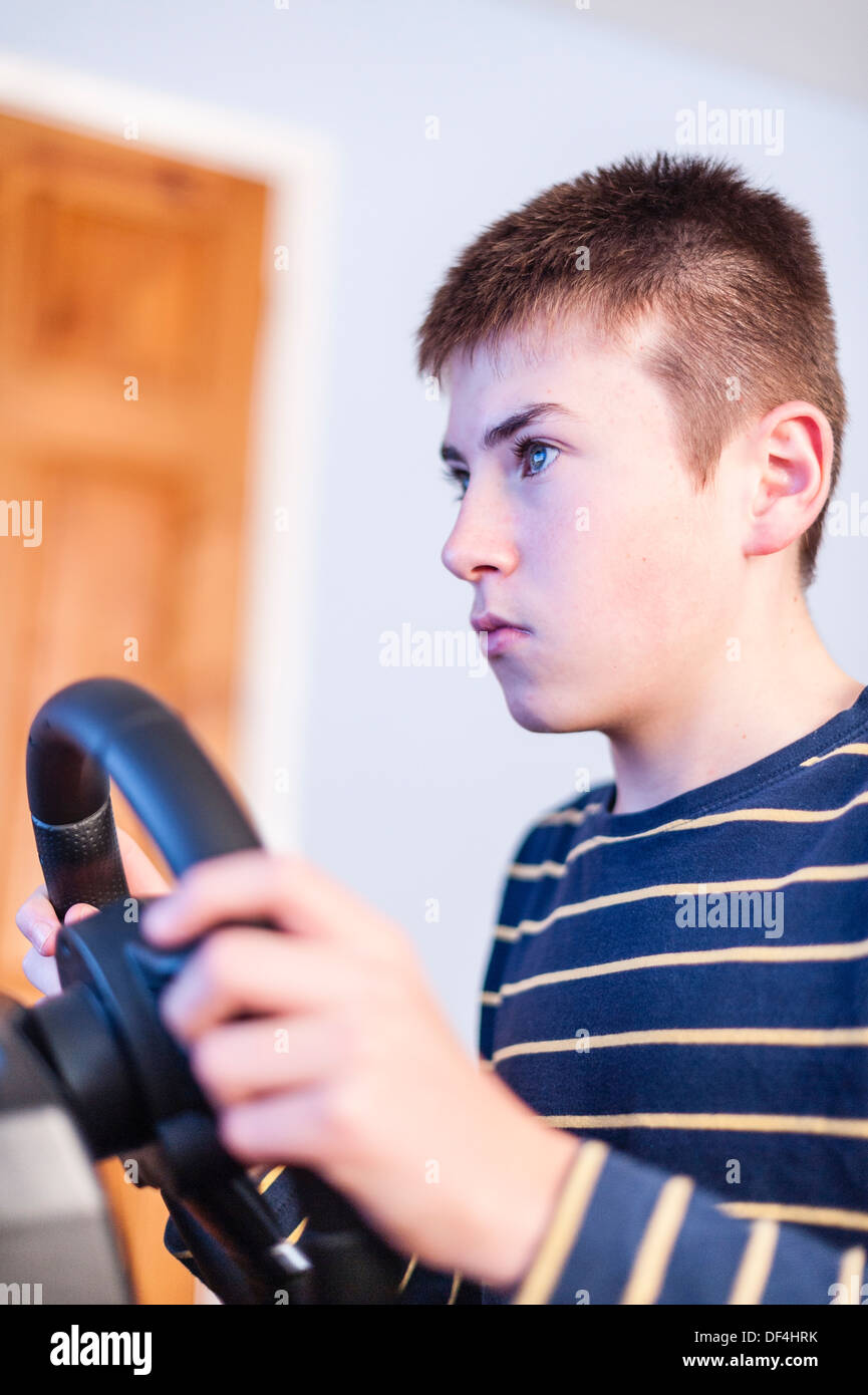 A 13 year old boy playing a computer driving game using a connected steering wheel in his bedroom Stock Photo