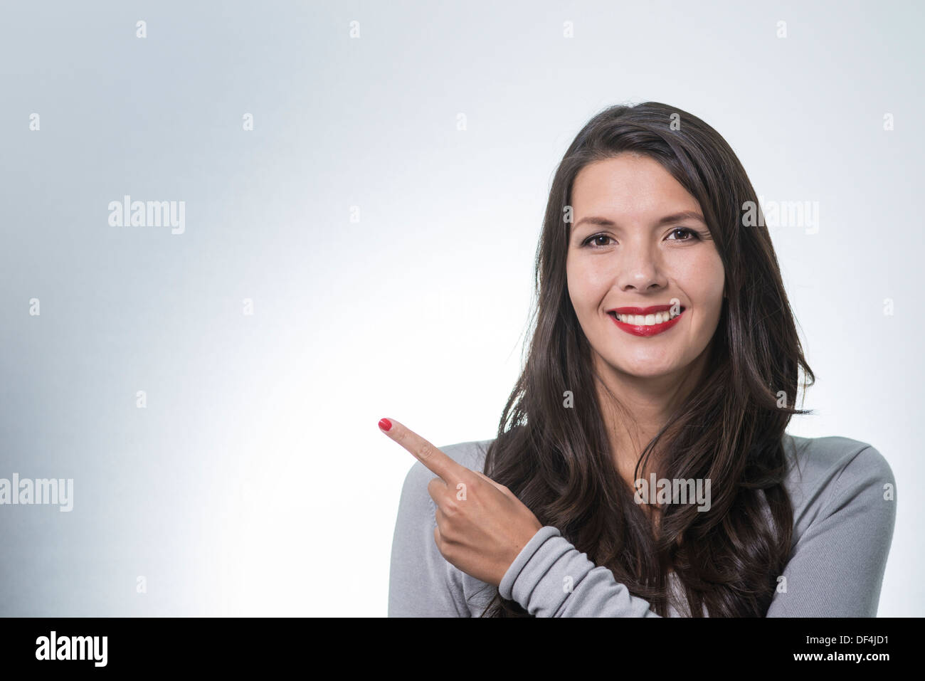 Beautiful young woman with a lovely friendly smile standing with an index finger pointing to copy space for your ad Stock Photo