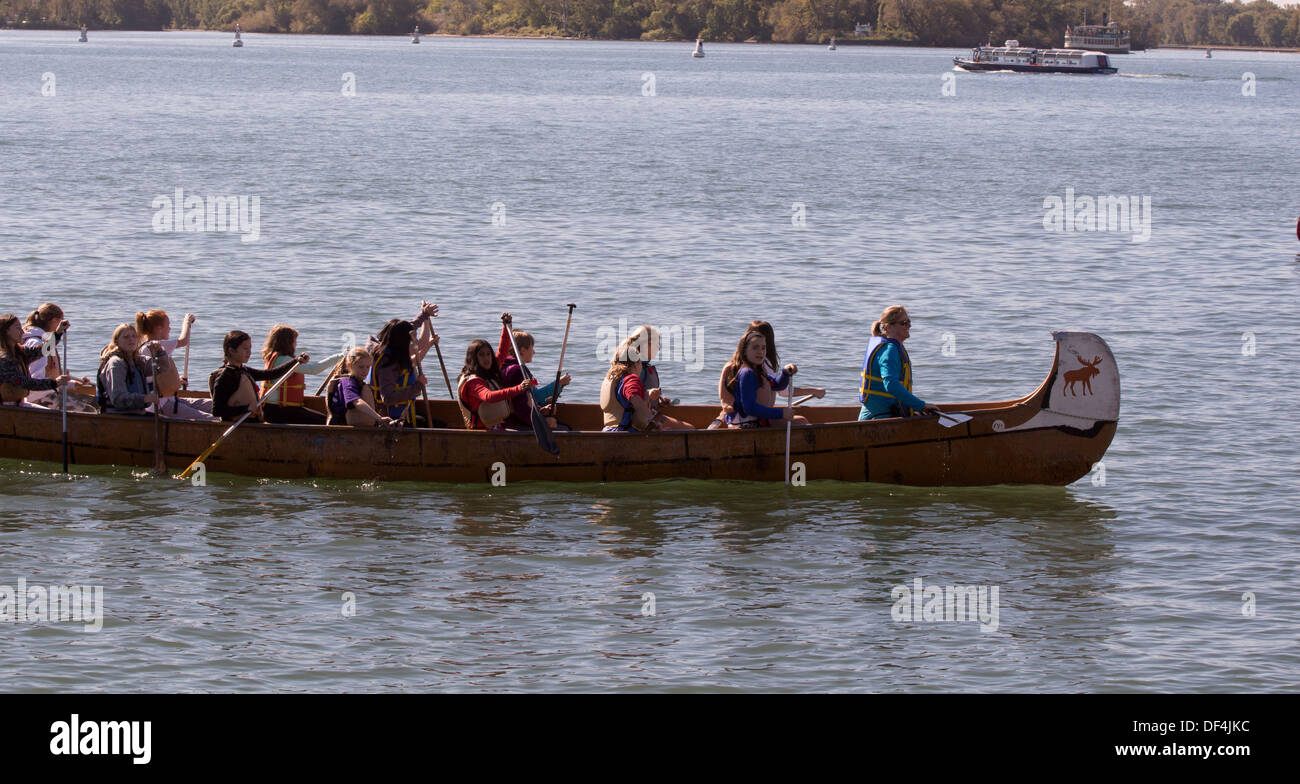 Women and teenagers wearing life jackets paddling and rowing a birch bark canoe on Lake Ontario with Moose on bow. Stock Photo