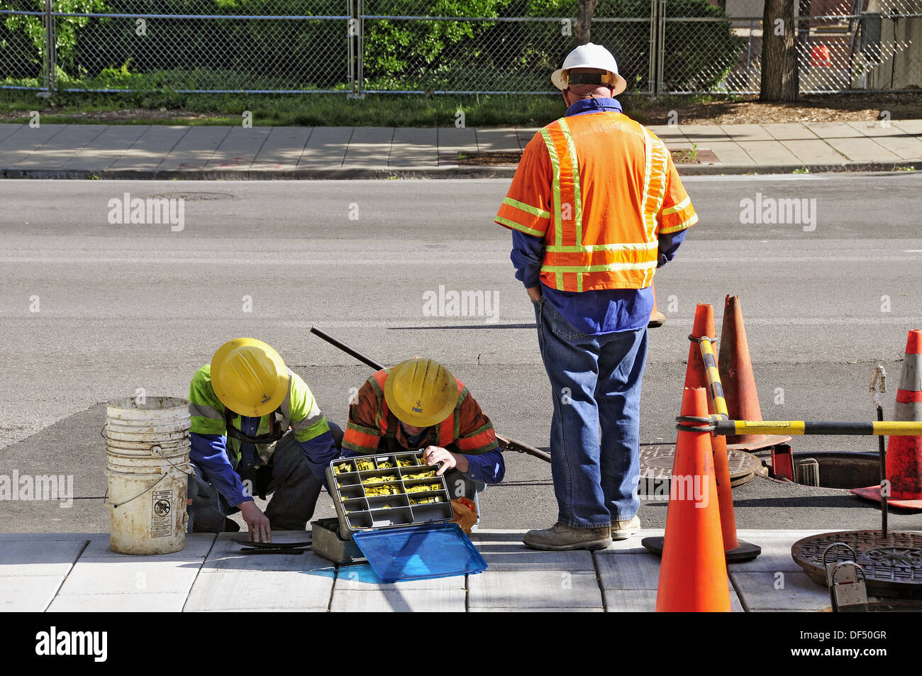 Utility workers prepare to work on and enter man hole in a city street