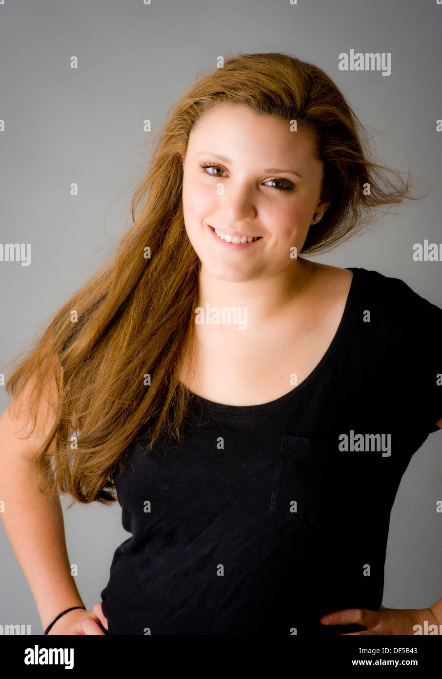 Young caucasian woman with long, light brown hair swept over her shoulder looking at camera smiling. Stock Photo