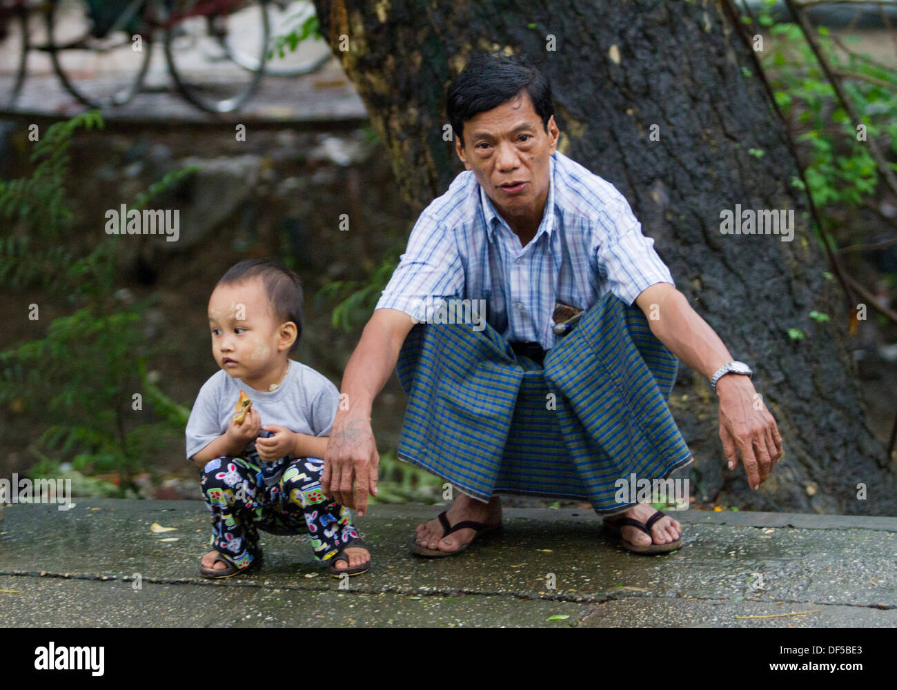 A father and son squat near a railway station in Yangon, Burma. Stock Photo