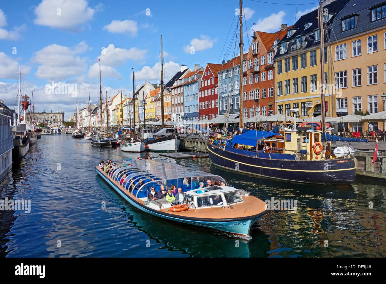 Colourful Nyhavn in Copenhagen Denmark with canal touring boat leaving for a tour round the harbour Stock Photo