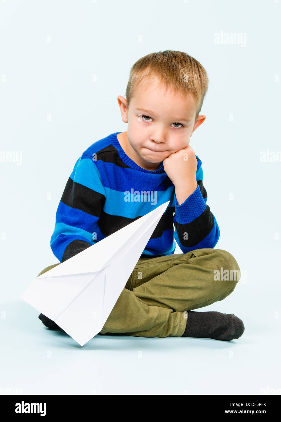 Happy boy playing with paper airplane in studio, light blue background ...