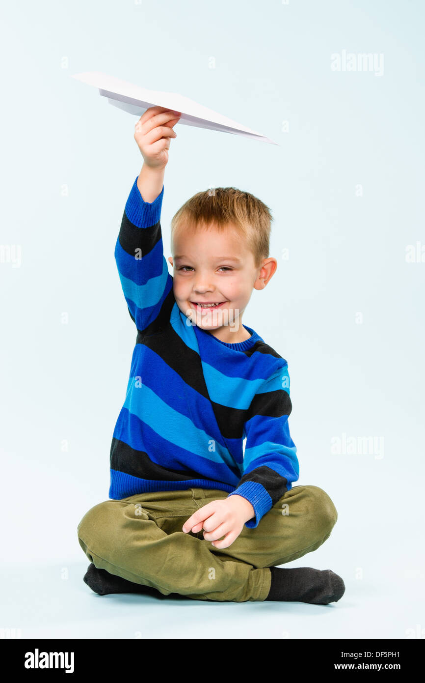 Happy boy playing with paper airplane in studio, light blue background ...