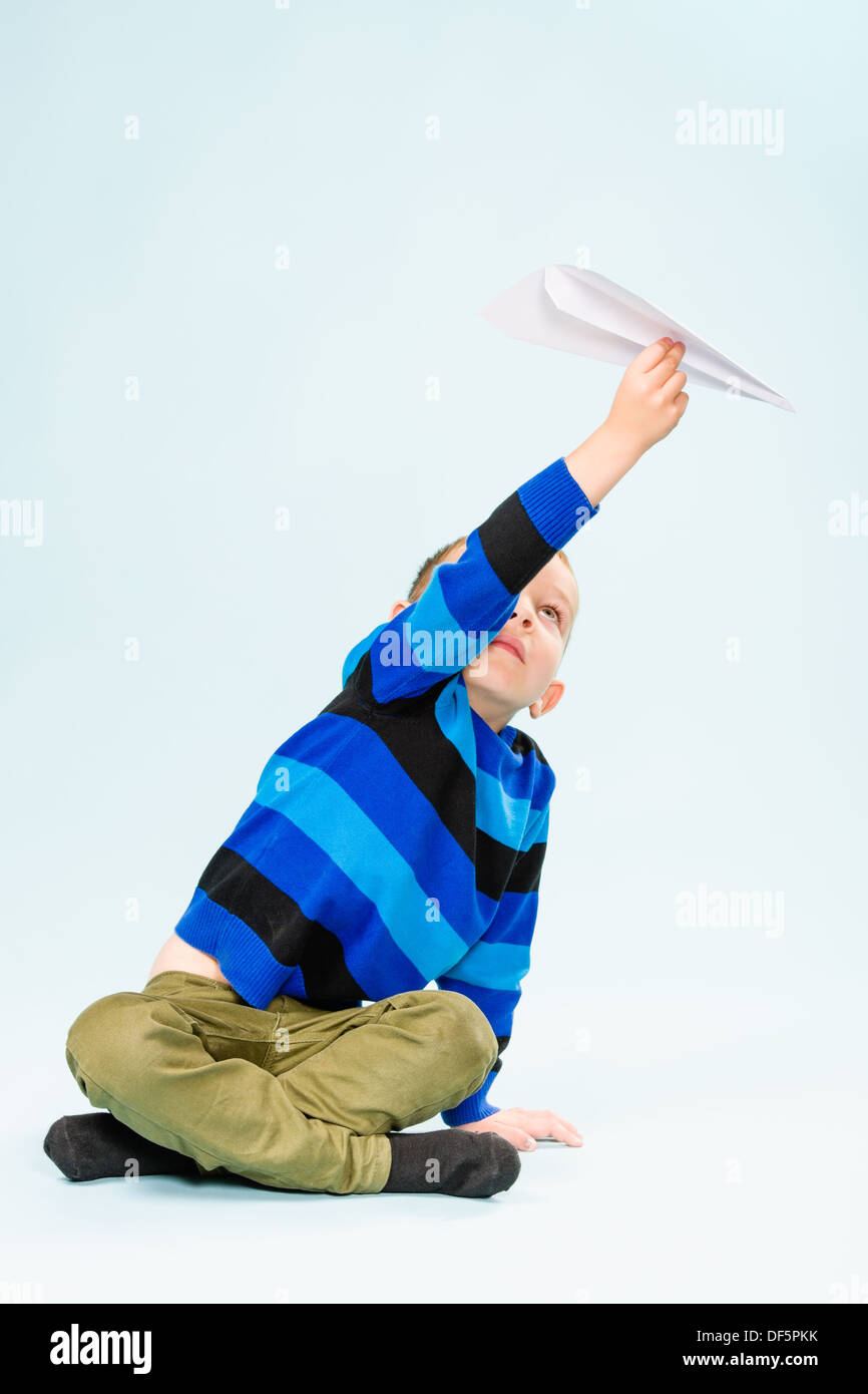 Happy boy playing with paper airplane in studio, light blue background ...