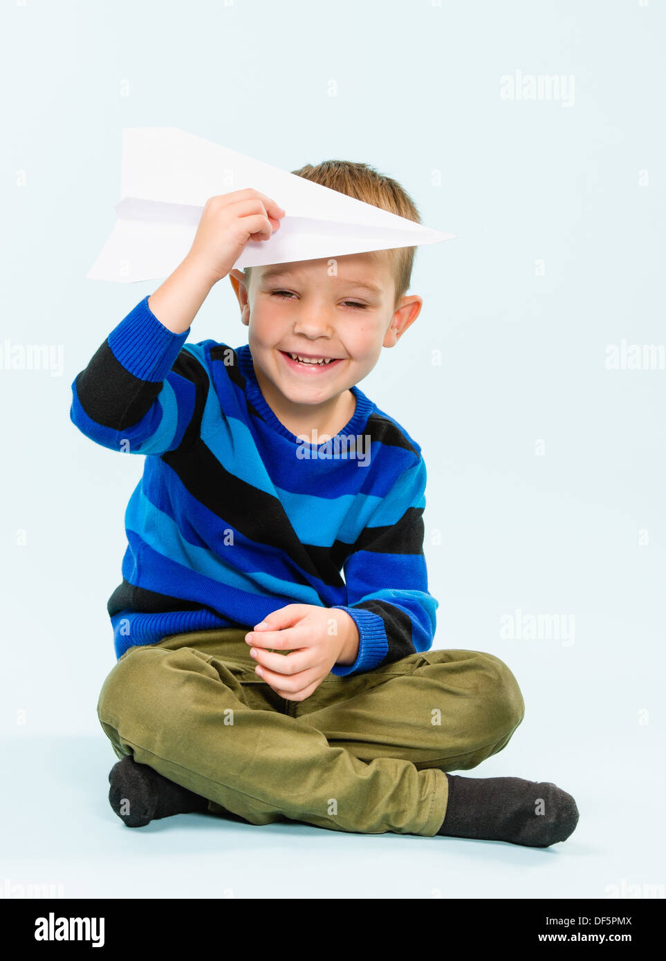 Happy boy playing with paper airplane in studio, light blue background ...