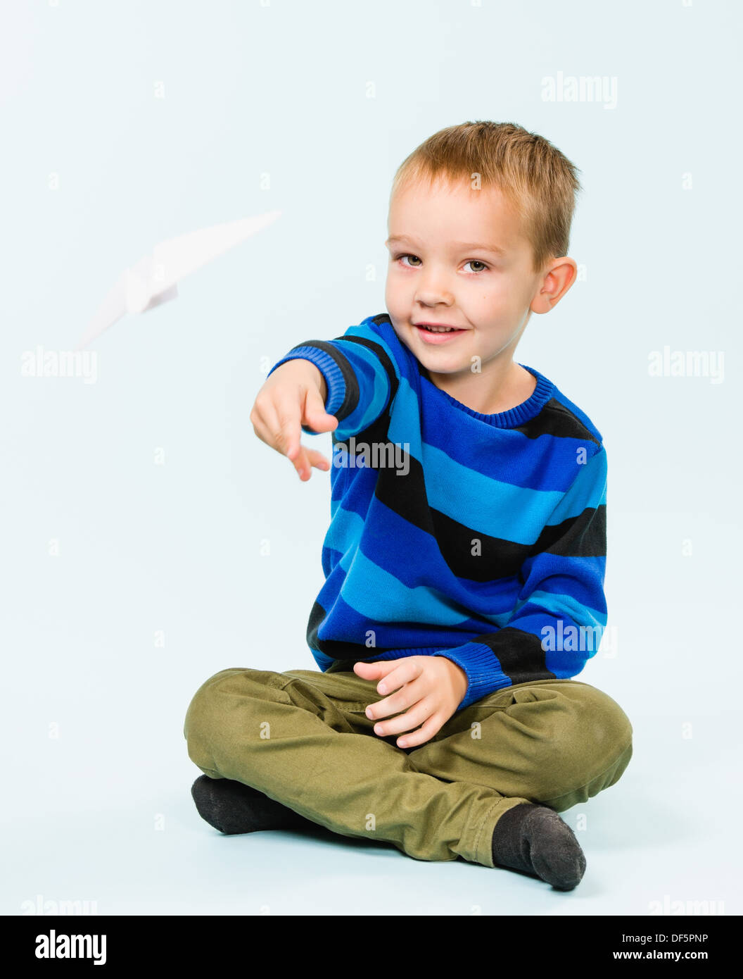 Happy boy playing with paper airplane in studio, light blue background ...