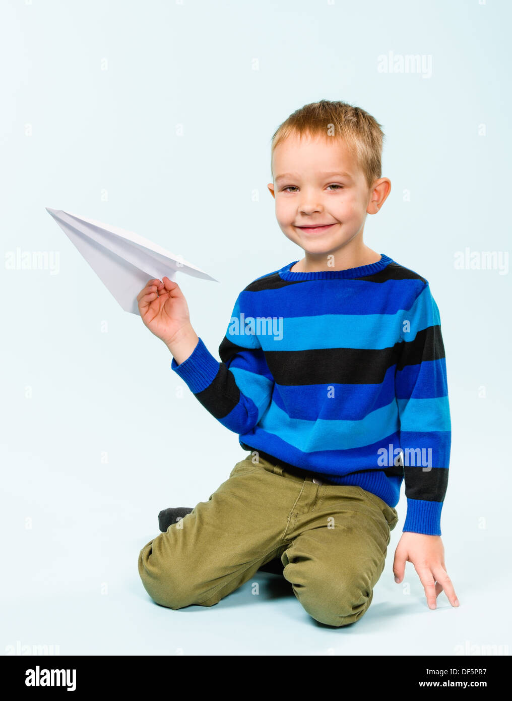 Happy boy playing with paper airplane in studio, light blue background ...