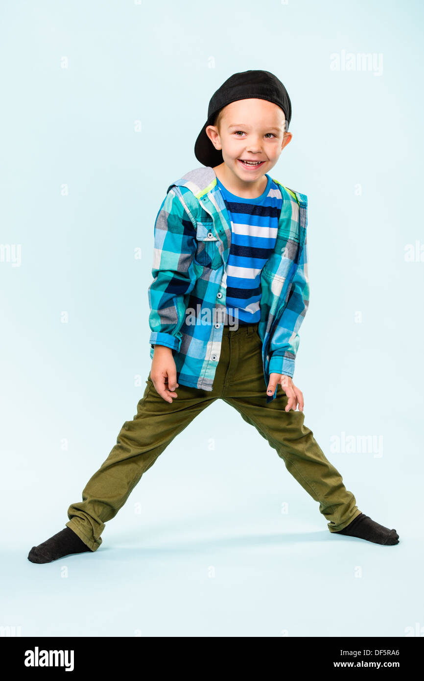 Playful little boy wearing peaked cap on studio, light blue background ...