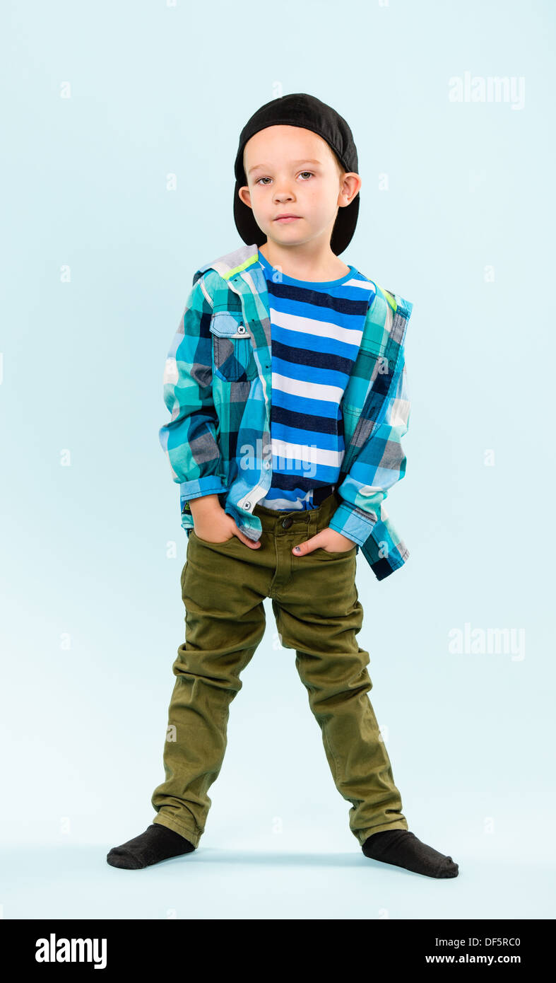 Playful little boy wearing peaked cap on studio, light blue background ...