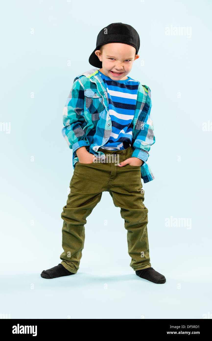 Playful little boy wearing peaked cap on studio, light blue background ...