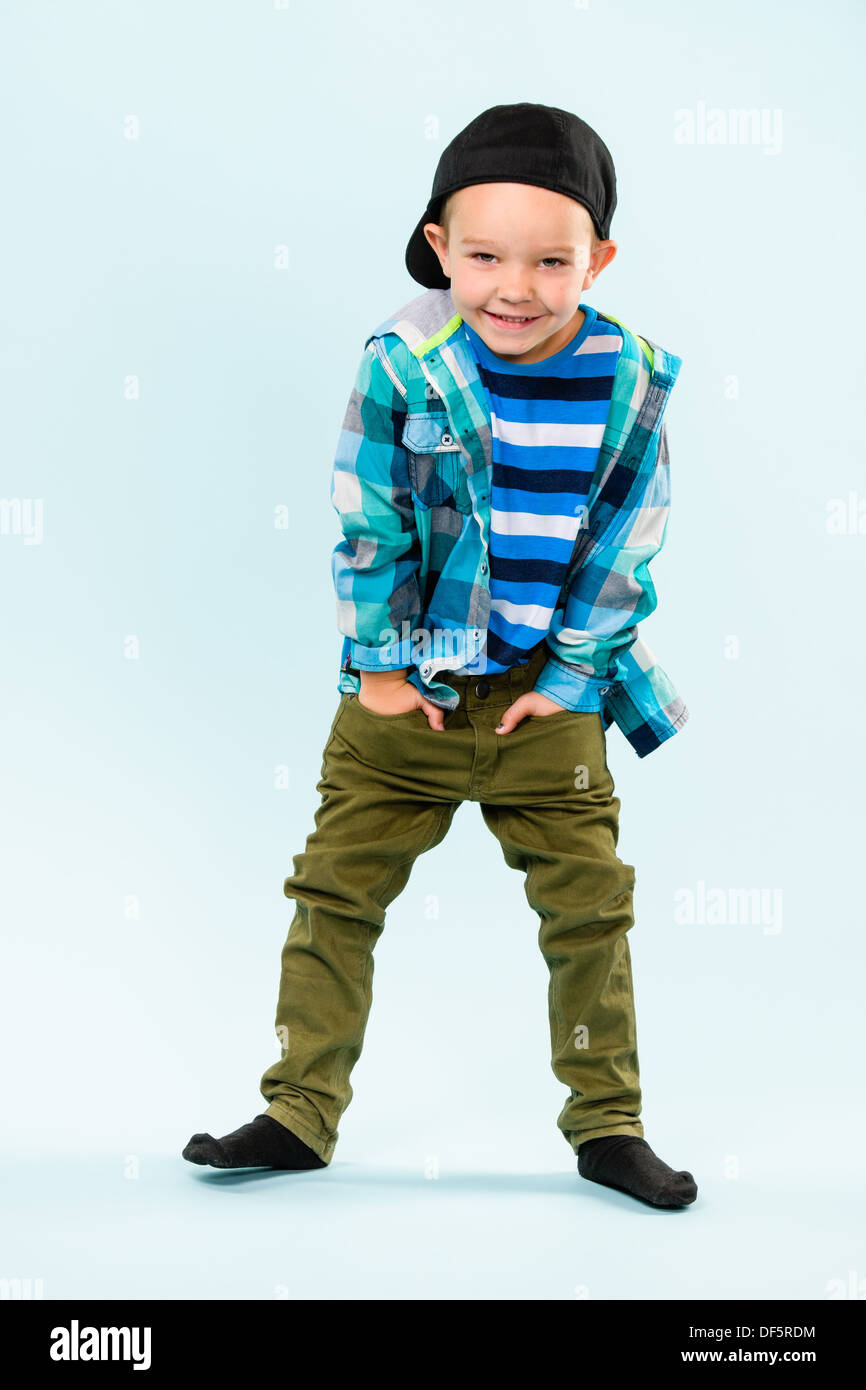 Playful little boy wearing peaked cap on studio, light blue background ...