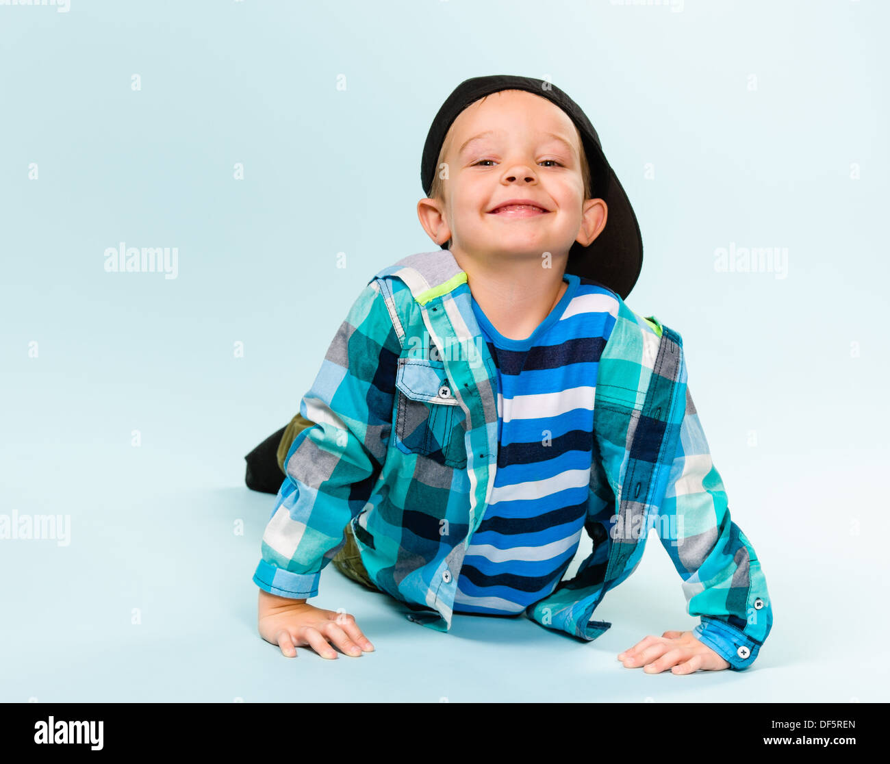 Playful little boy wearing peaked cap on studio, light blue background ...