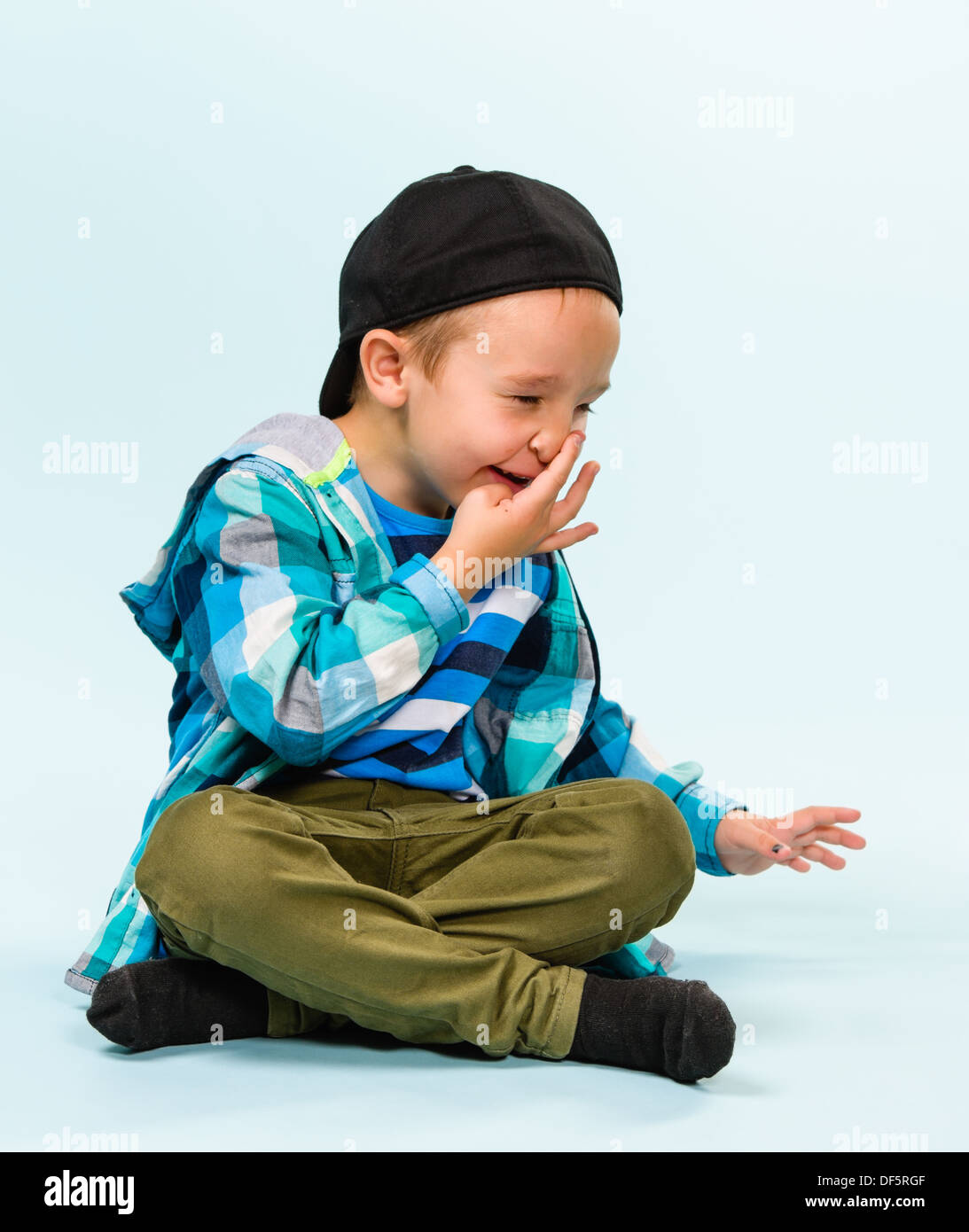 Playful little boy wearing peaked cap on studio, light blue background ...