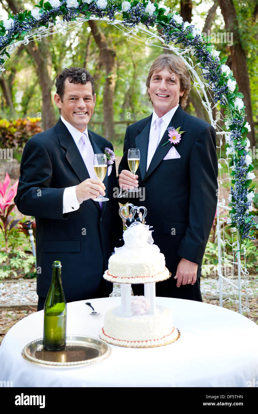Handsome gay couple toasting with champagne at their beautiful outdoor wedding reception.  Stock Photo