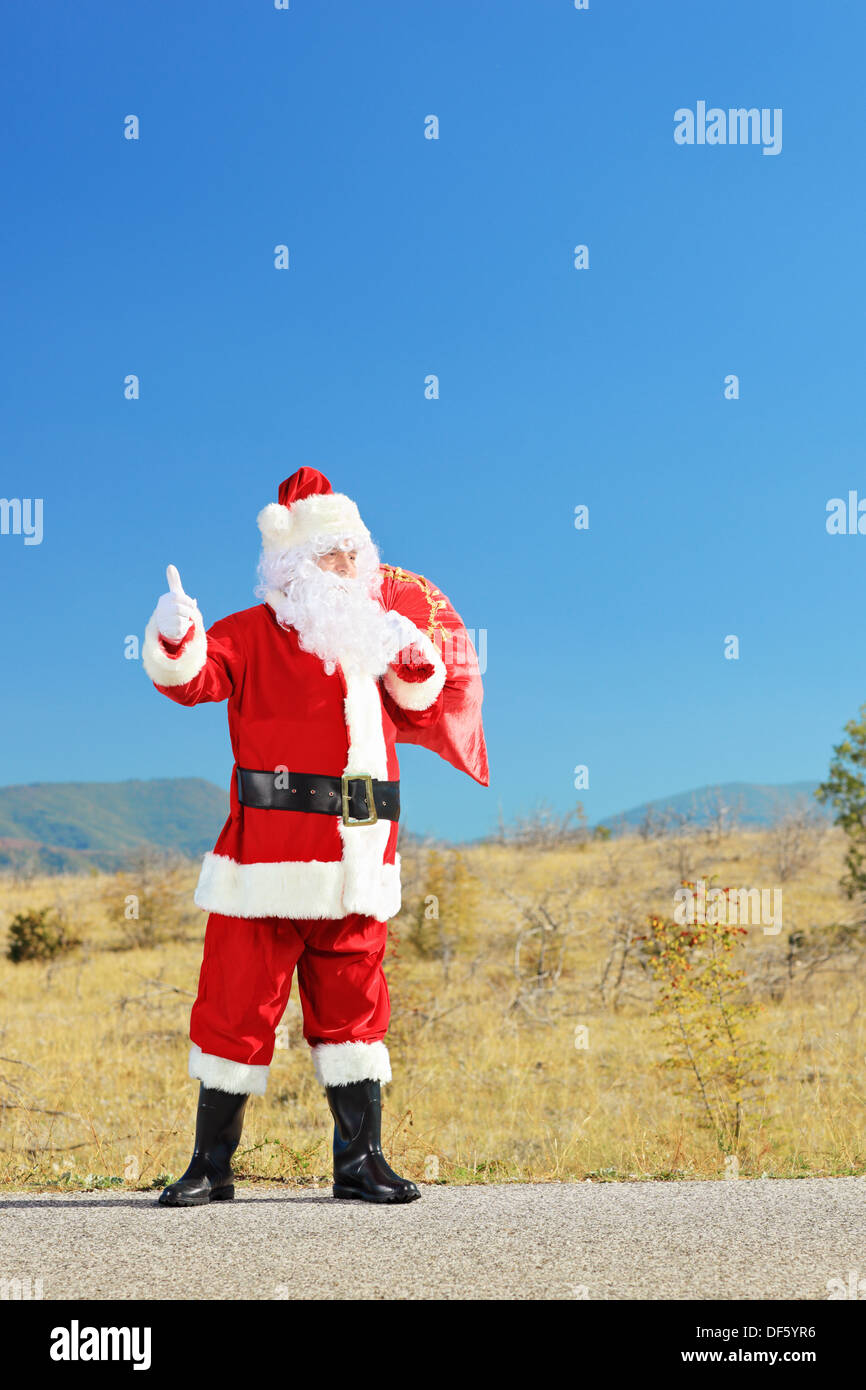 Santa Hitching A Ride Full length portrait of a santa claus with bag on an open road ...