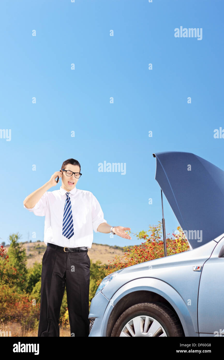 Young businessman standing near a broken car and talking on a phone Stock Photo