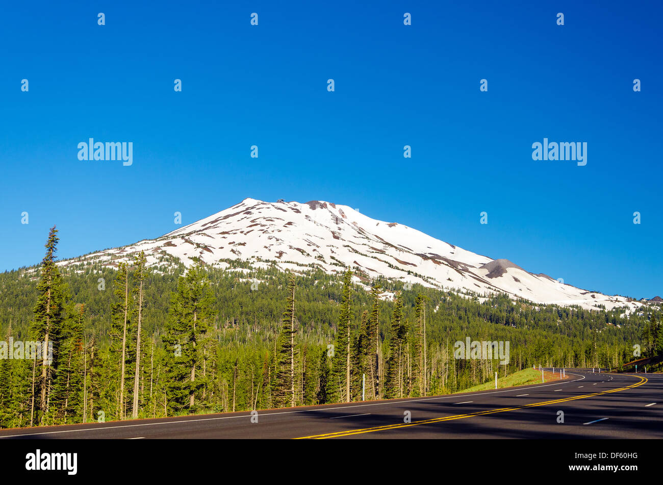 A highway leading through a forest passing next to snowy Mount Bachelor near Bend, Oregon Stock Photo