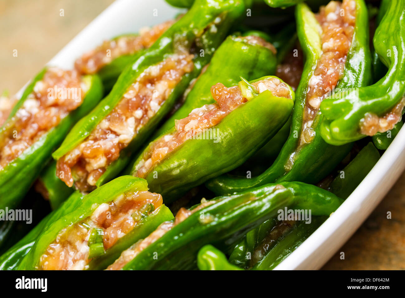 Closeup tilted horizontal photo of uncooked fresh, stuffed green sweet peppers, in white bowl, on stone counter top Stock Photo