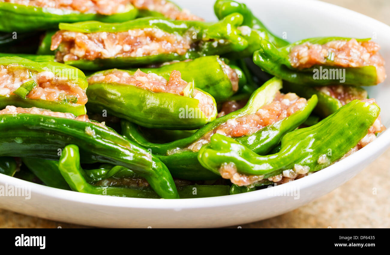 Closeup horizontal photo of uncooked fresh, stuffed green sweet peppers in white bowl on stone counter top Stock Photo