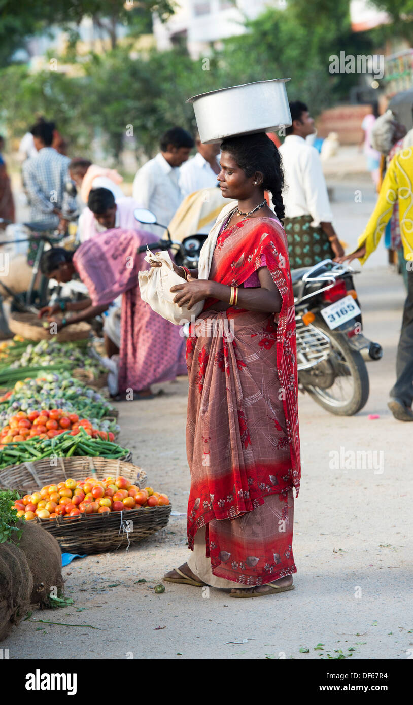 Poor lower caste Indian woman at a street market carrying a pot of rice on her head collecting the unsellable food. Andhra Pradesh, India Stock Photo