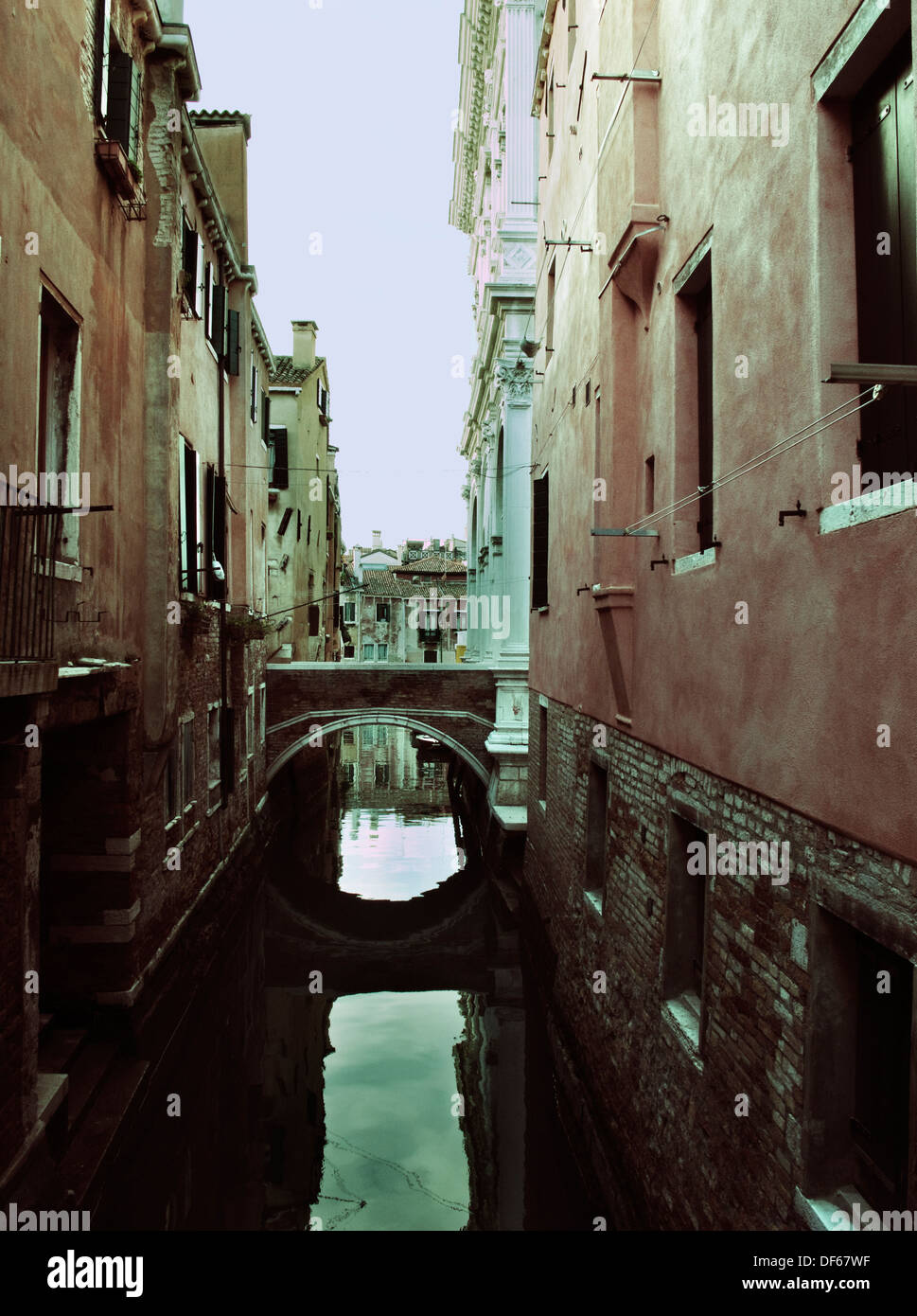 Narrow canal and small bridge between houses, Venice, Italy, cross processed Stock Photo