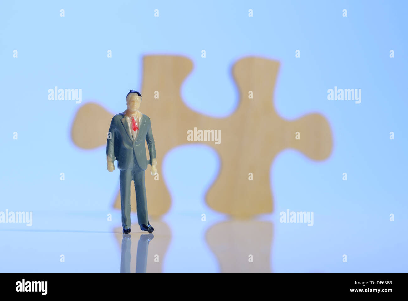 Plastic business man standing in front of a wooden jigsaw piece Stock Photo