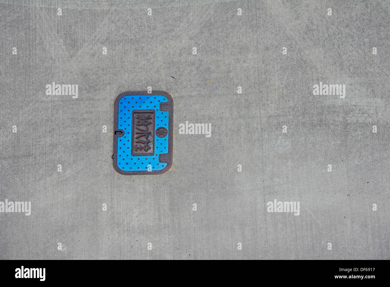 Man hole cover in blue with Japanese inscription mounted in a concrete jetty. Stock Photo