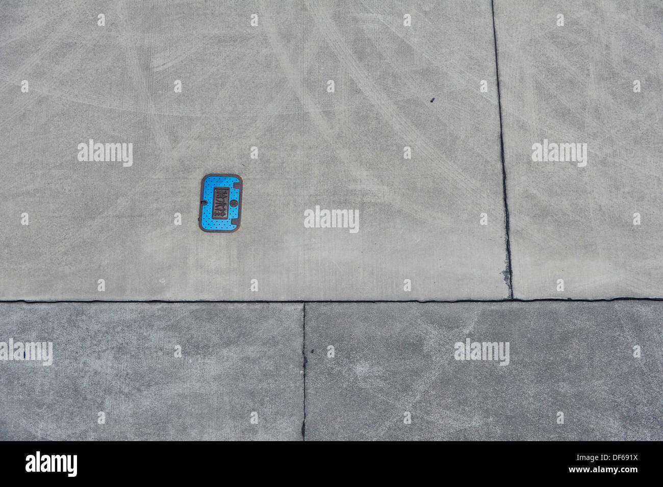 Man hole cover in blue with Japanese inscription mounted in a concrete jetty. Stock Photo