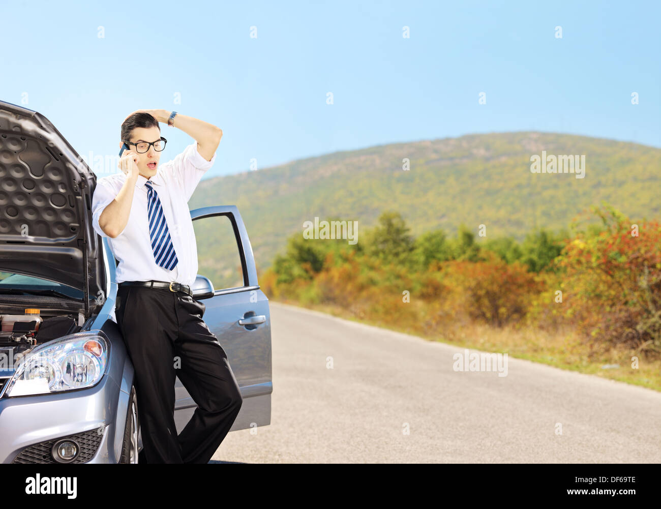 Young sad male on a broken car talking on a cell phone Stock Photo